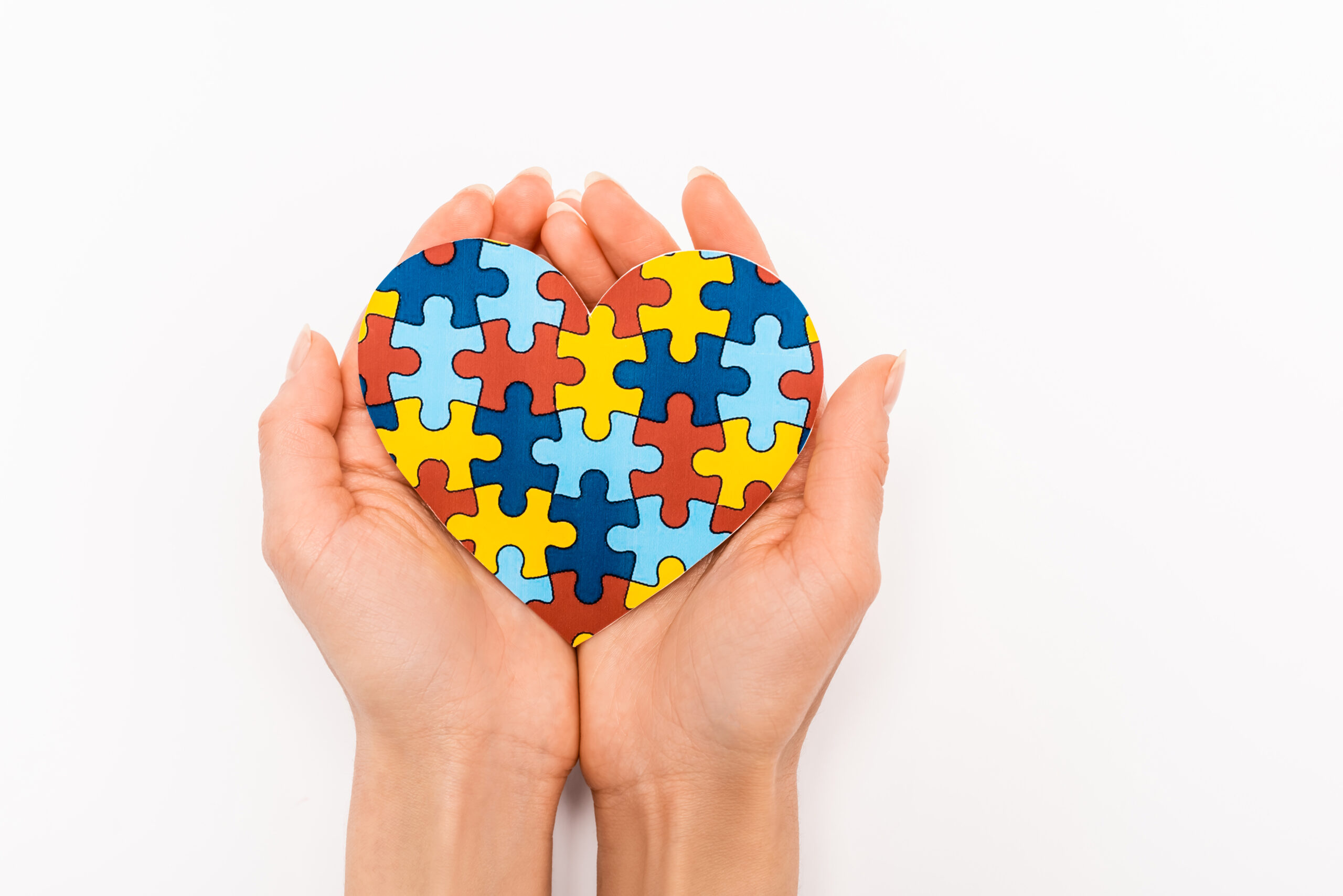 Cropped view of puzzle heart in female hands on white background, autism concept