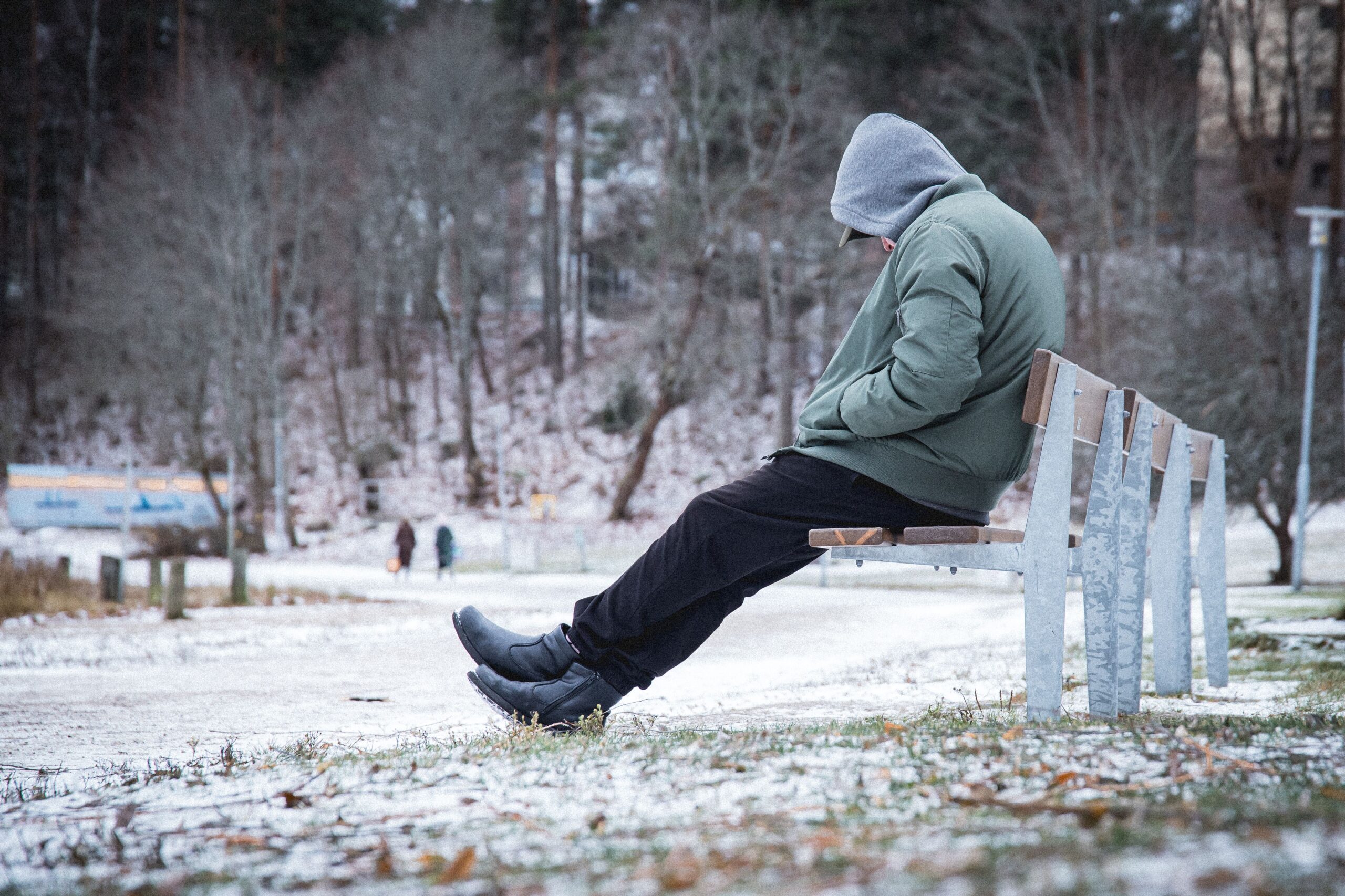 A lonely man sitting on the bench in a snowy park