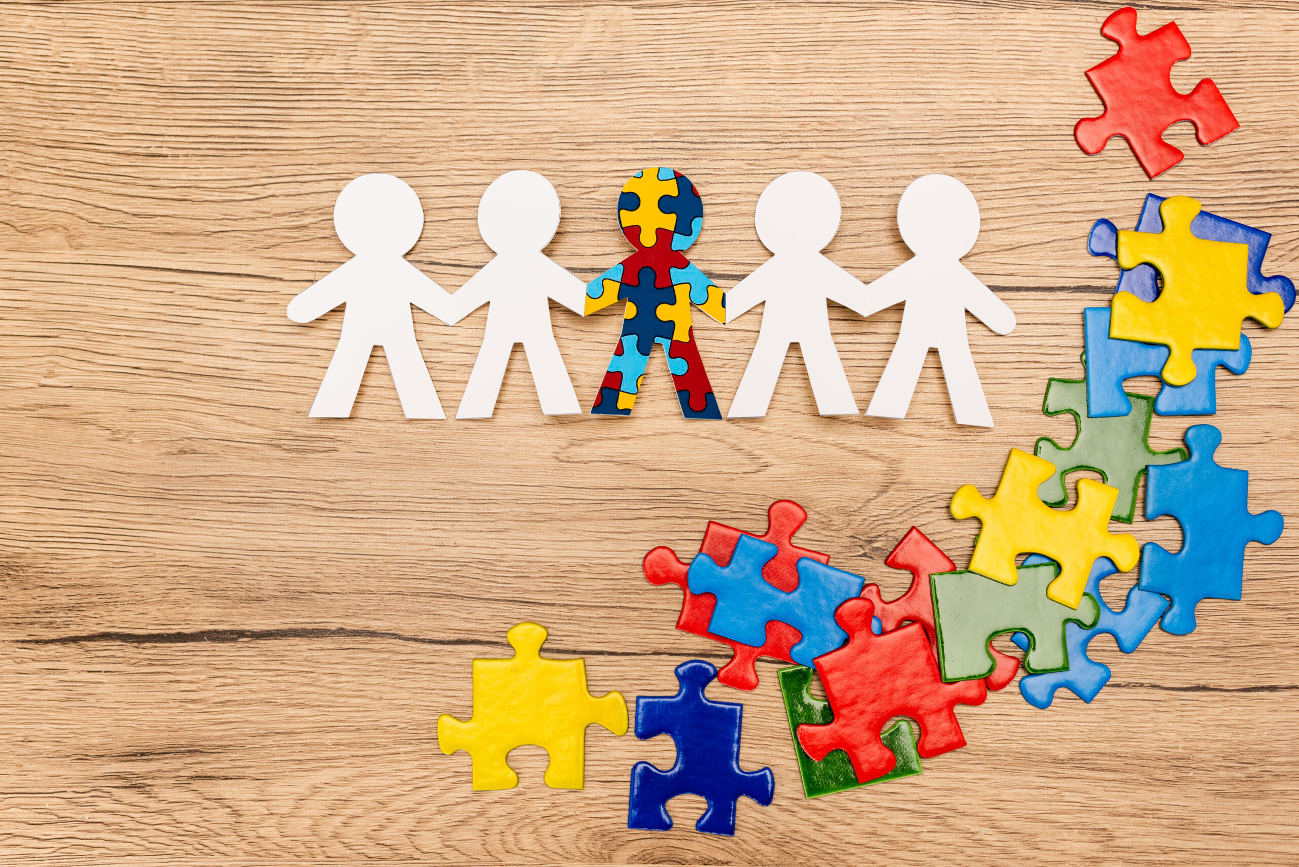 Top view of special kid with autism among another and pieces of bright colorful puzzle on wooden