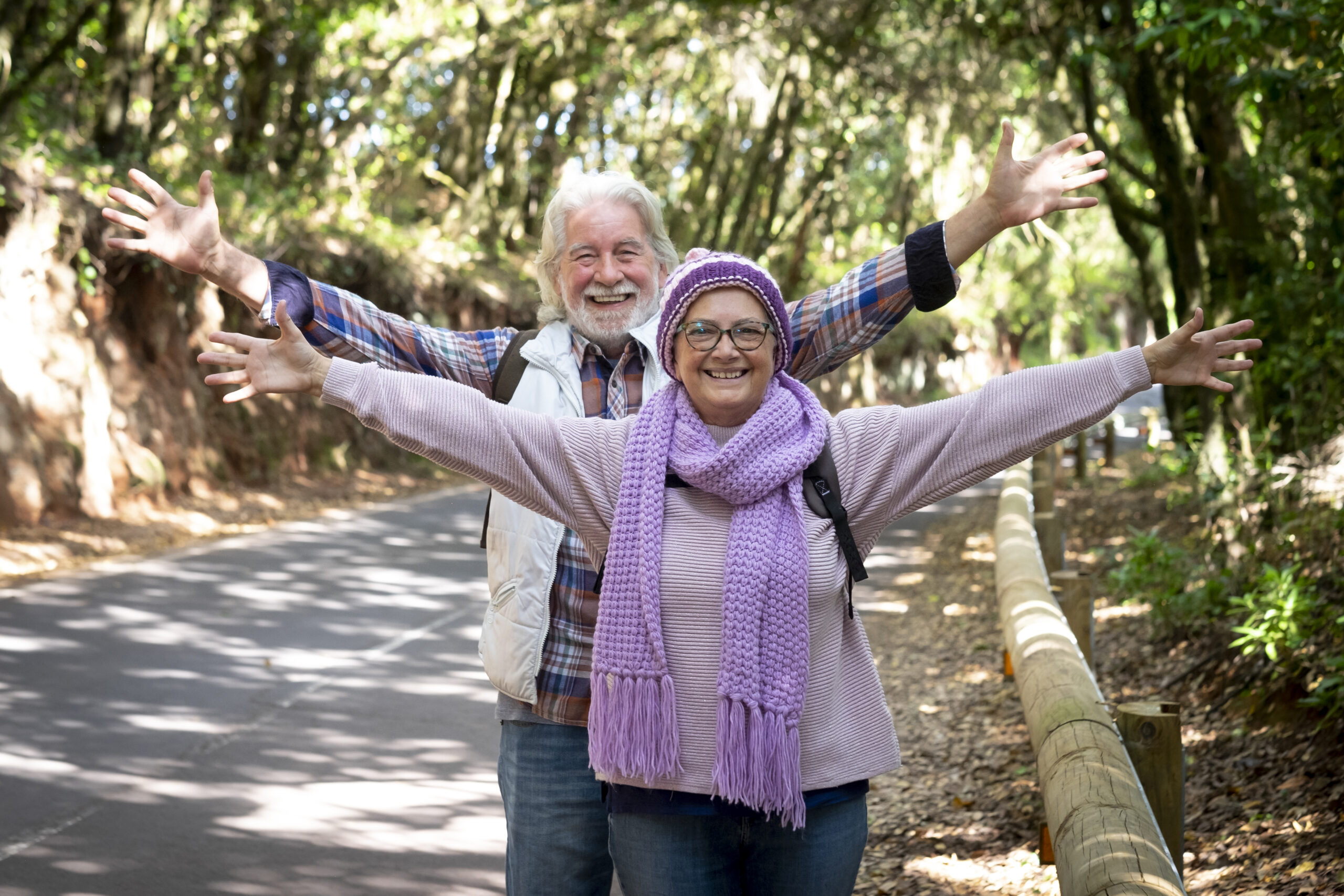 Smiling happy senior couple with raised arms looking at camera enjoying mountain excursion in a winter day. Active retired elderly people and fun concept