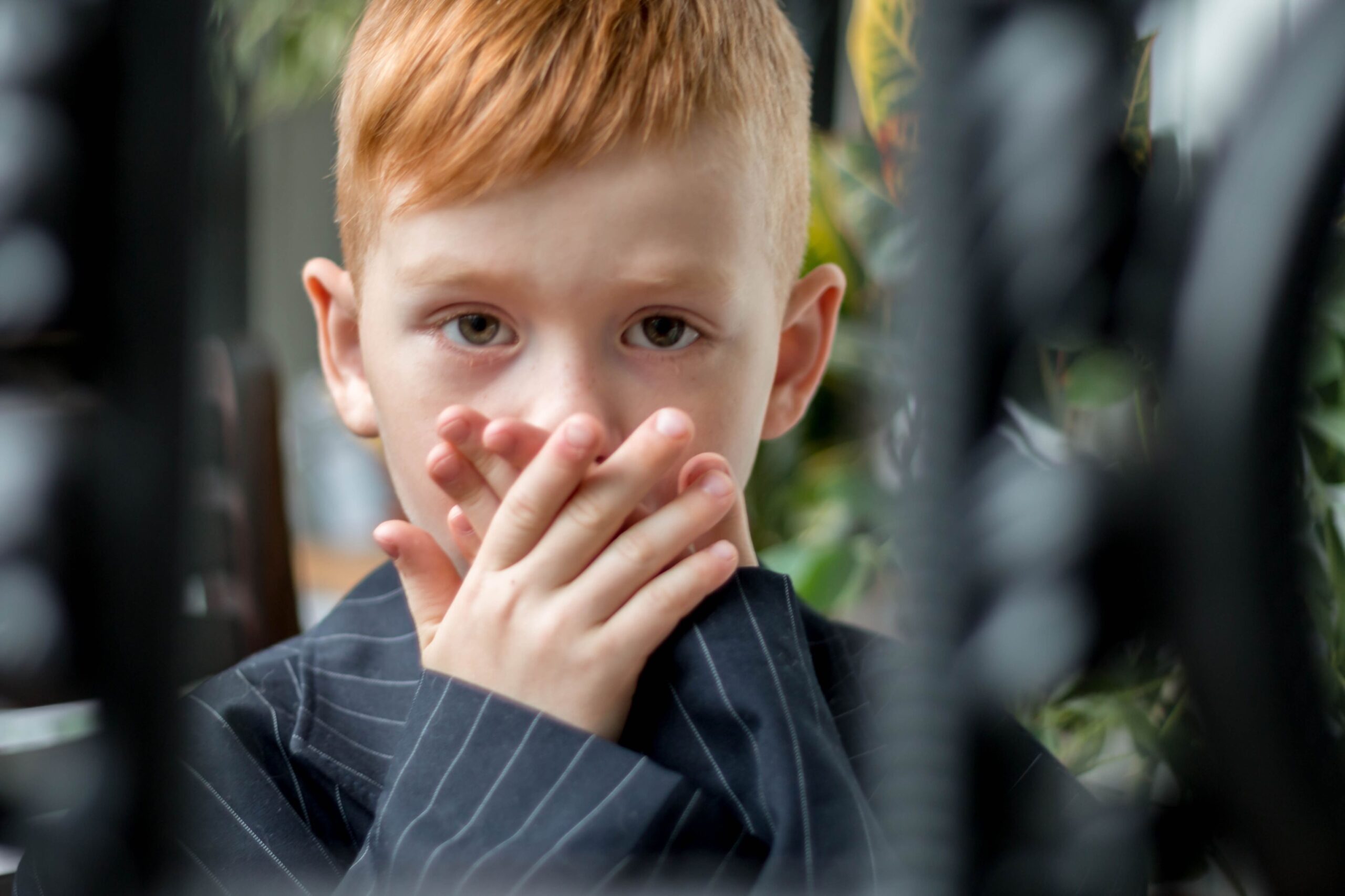 anxious little boy with red hair putting his hands over his mouth