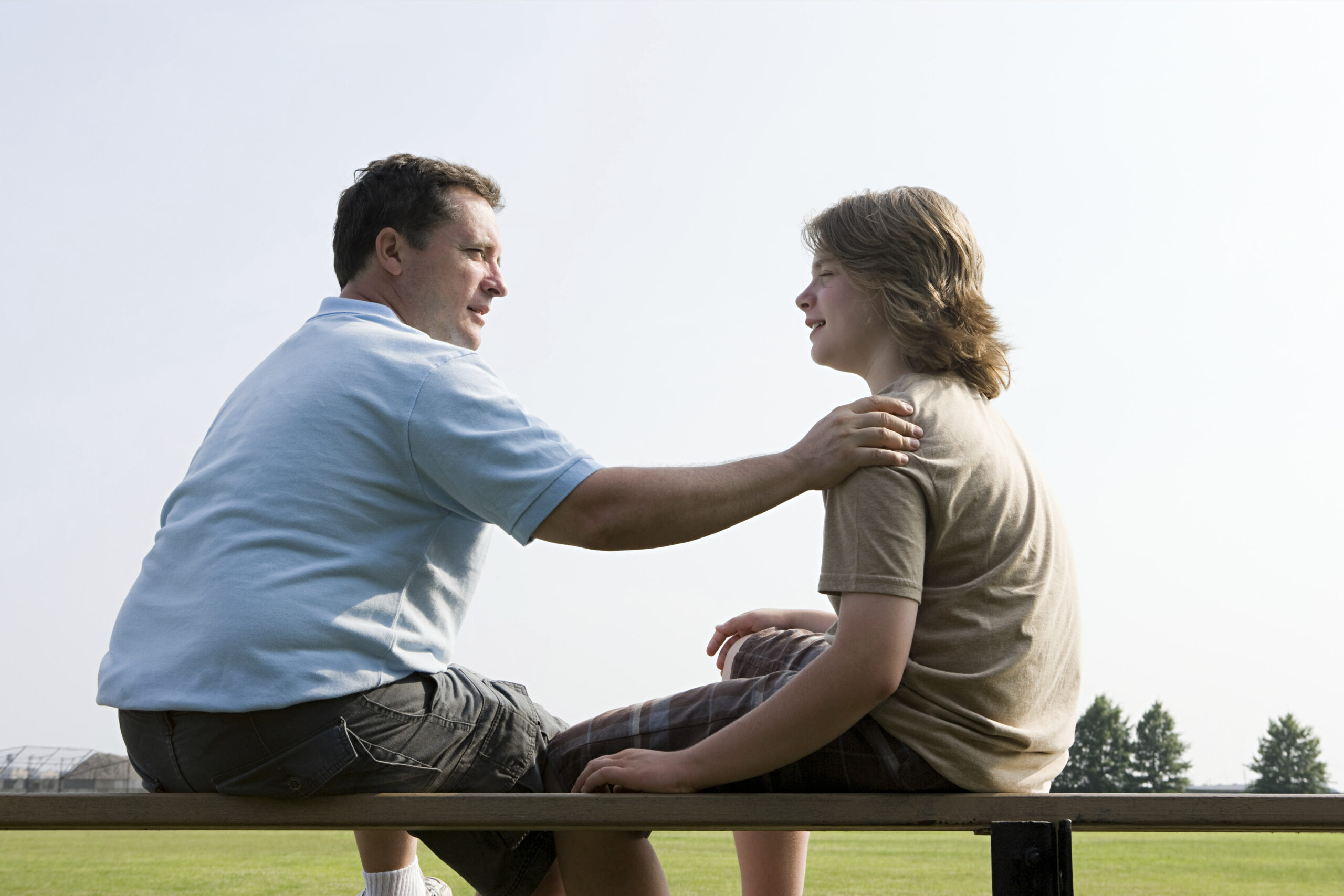 Father and son having a heartfelt conversation on a park bench.