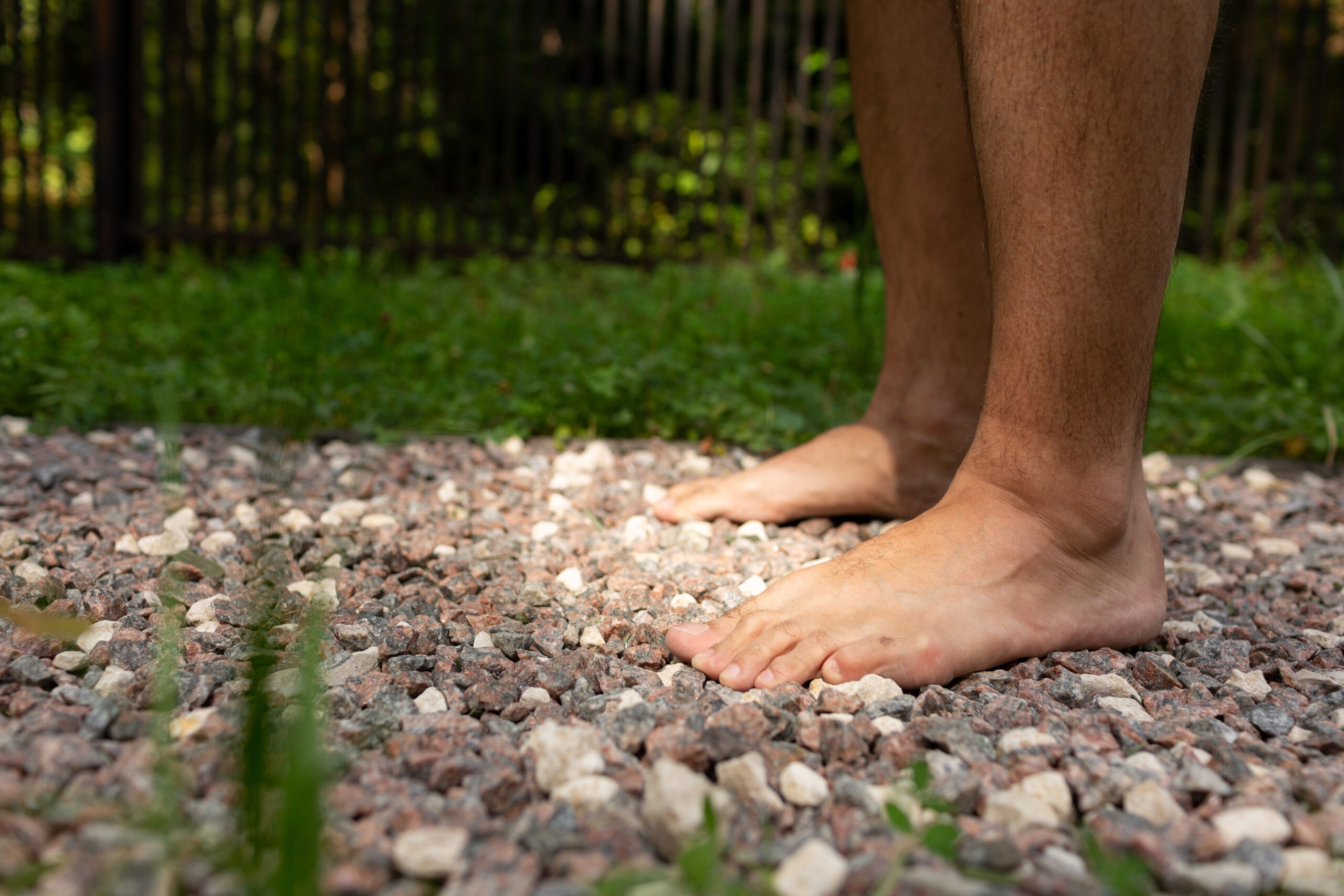 A man stands barefoot on a path of fine gravel