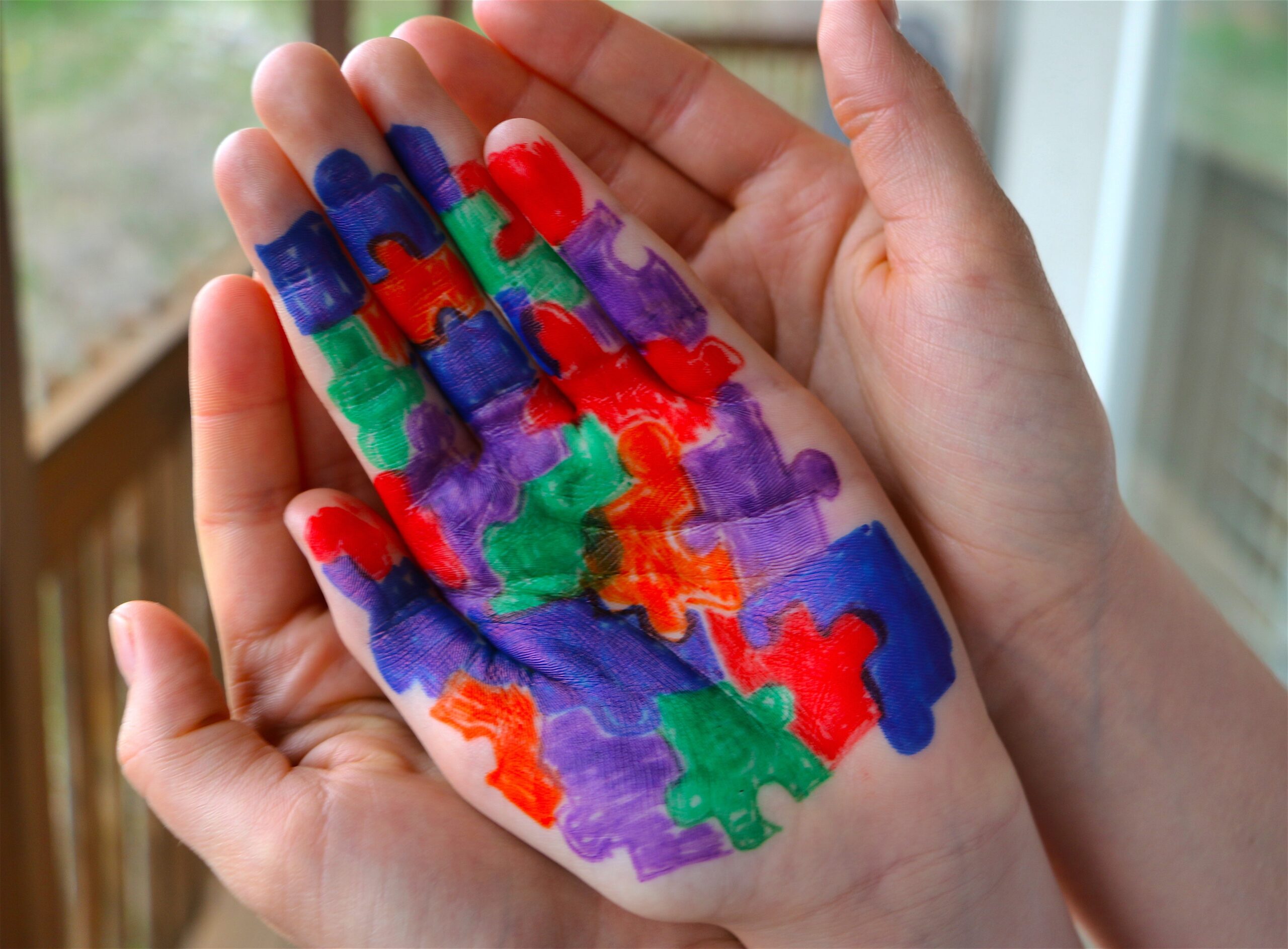 mother holding childs hands with autism symbol painted on the childs hands