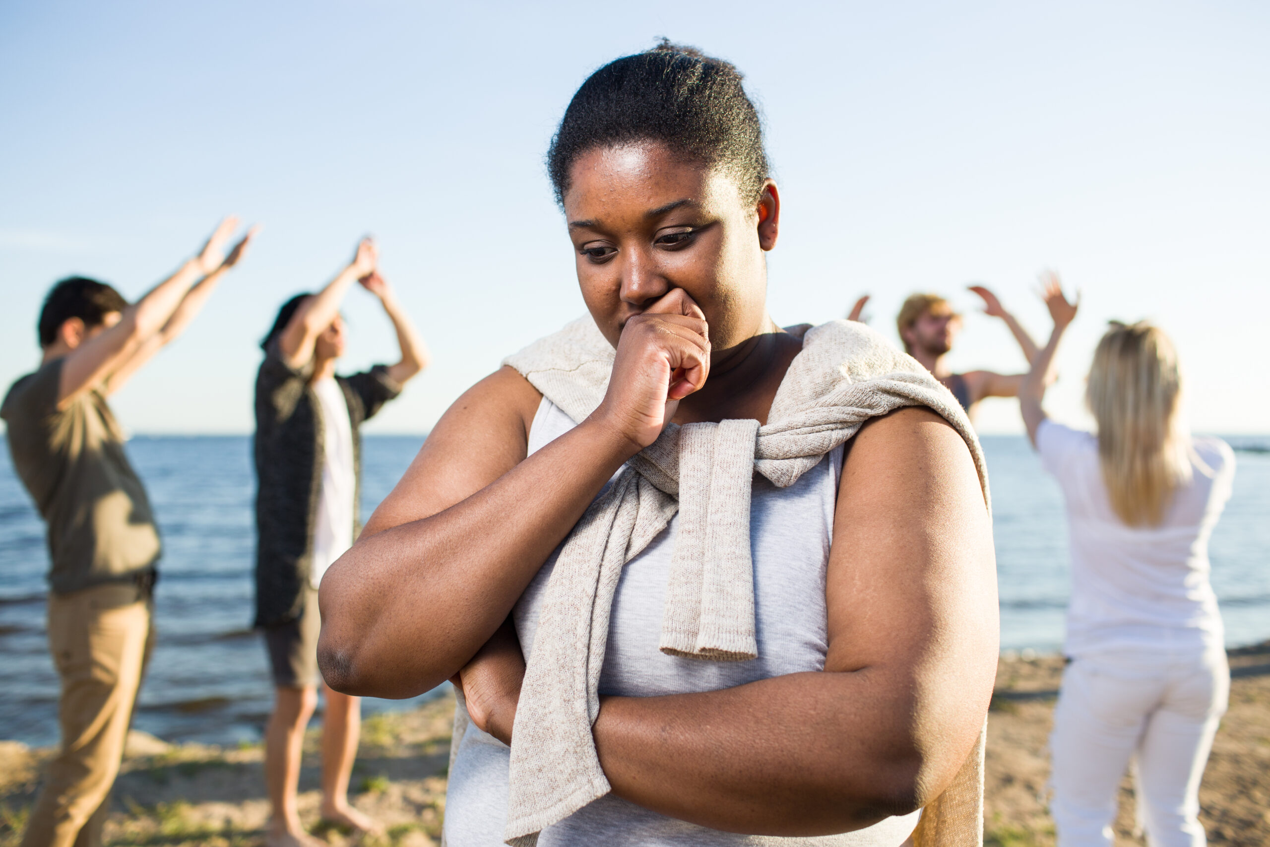 Thoughtful girl is unsure about dancing with her friends at beach party