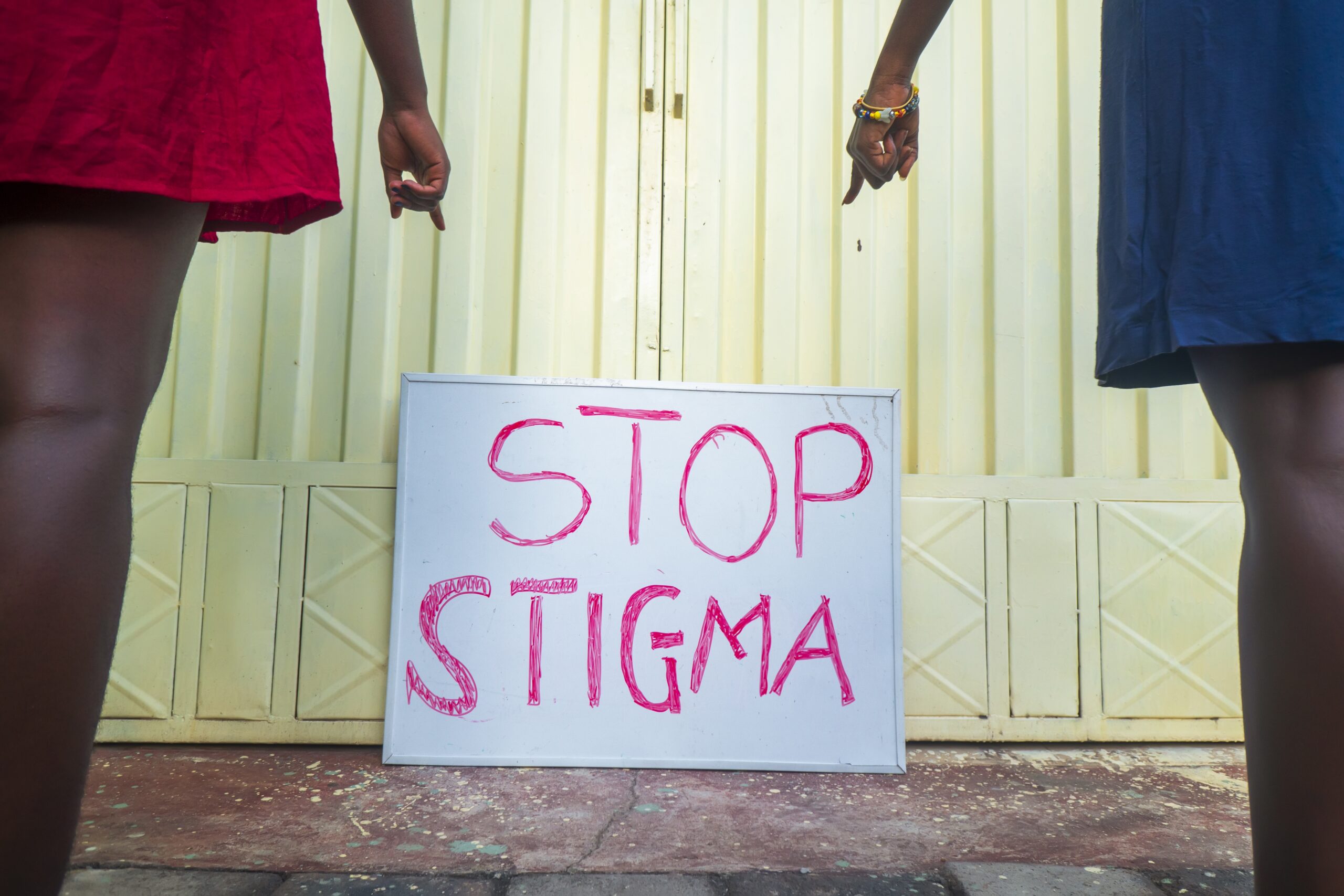 A horizontal shot of two African American women pointing at a sign "Stop Stigma" - no to stereotypes