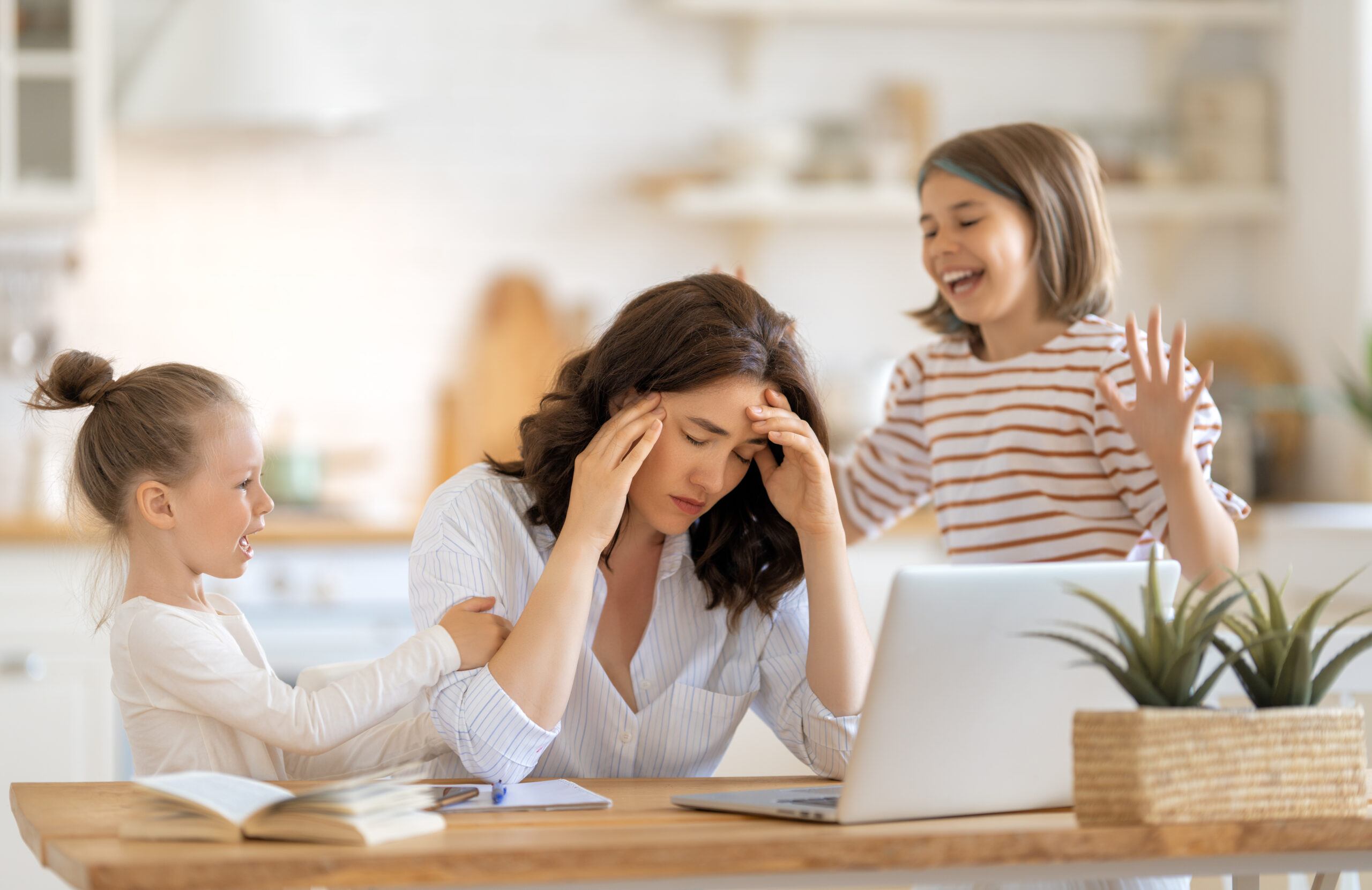 Woman working on a laptop. Noisy children and remote work from home.