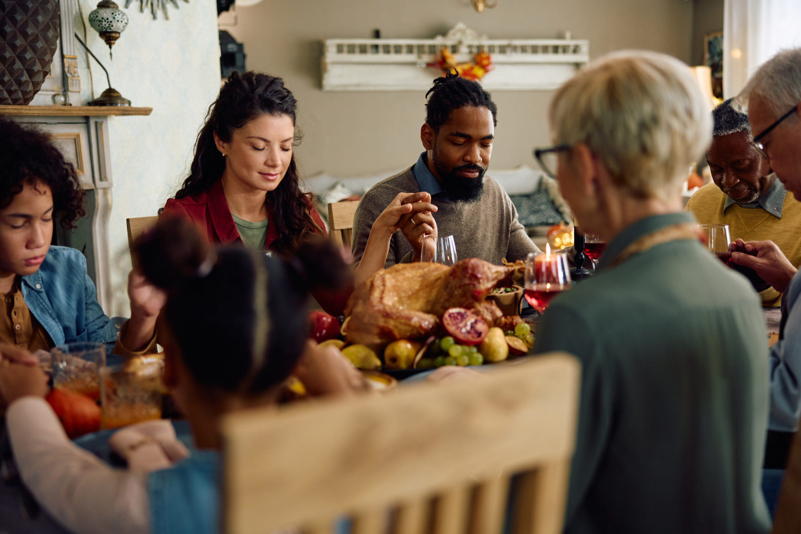 Extended family saying grace while gathering for meal at dining table on Thanksgiving.