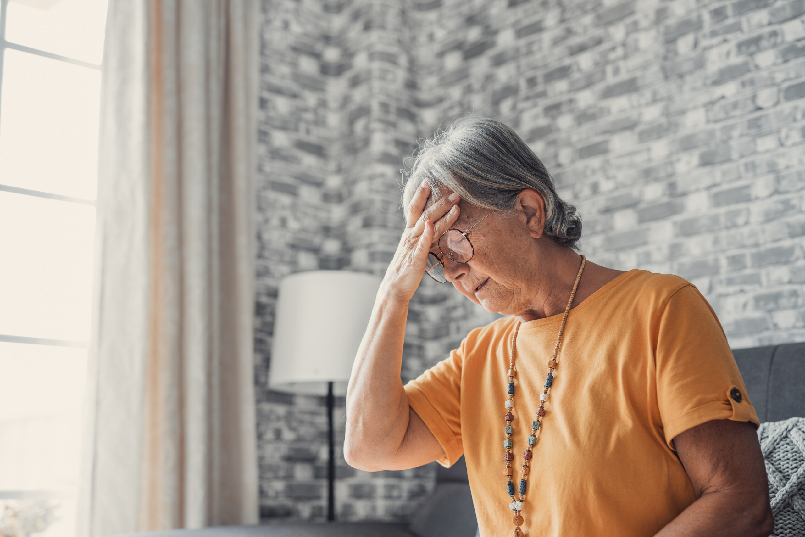 Sad depressed middle aged mature woman sitting alone at home touching head feeling headache migraine, upset tired old senior lady widow mourning suffer from grief loneliness mental problems concept