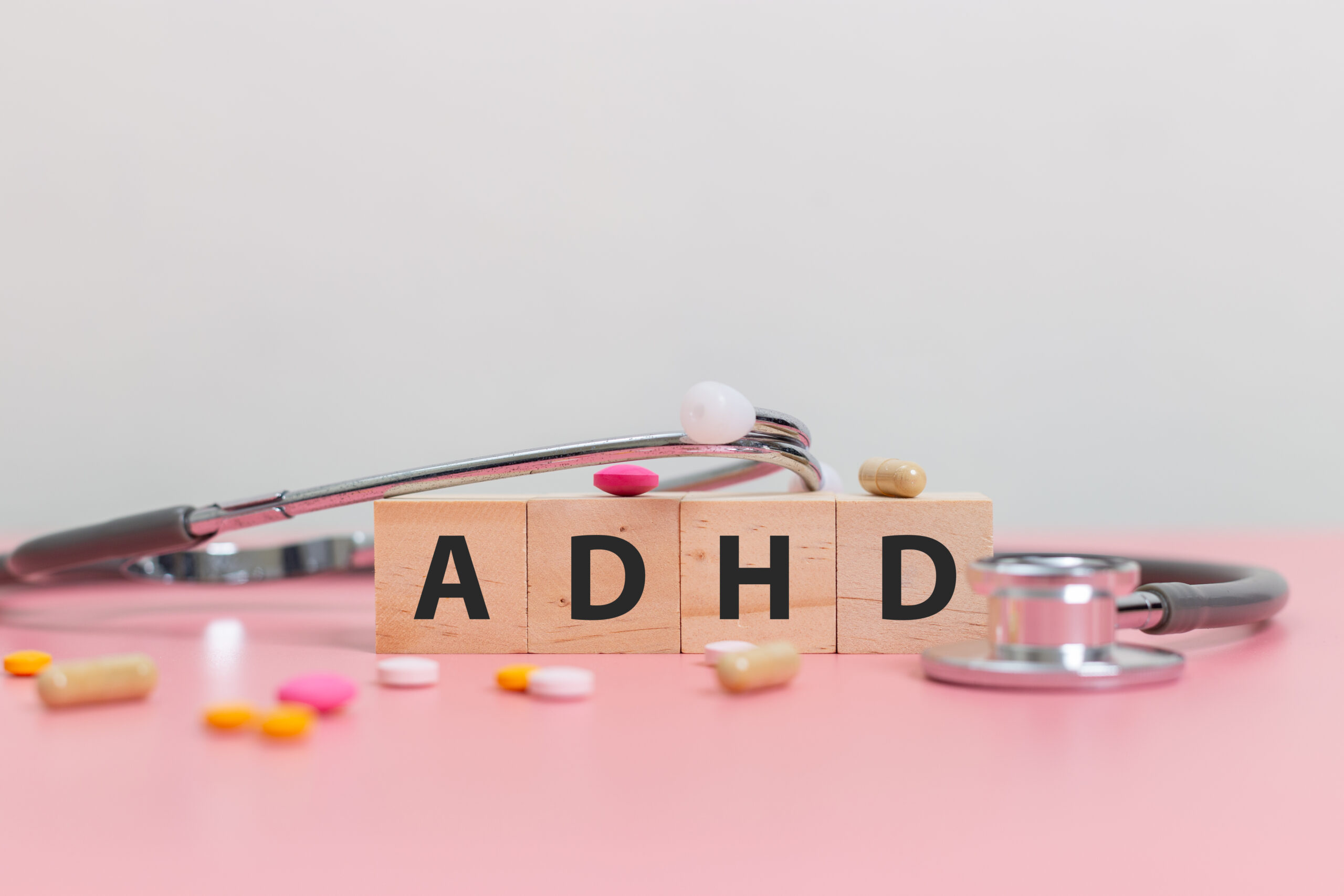 wood cube block Abbreviation of ADHD with Stethoscope and pills on pink table. Attention Deficit Hyperactivity Disorder. ADHD concept.