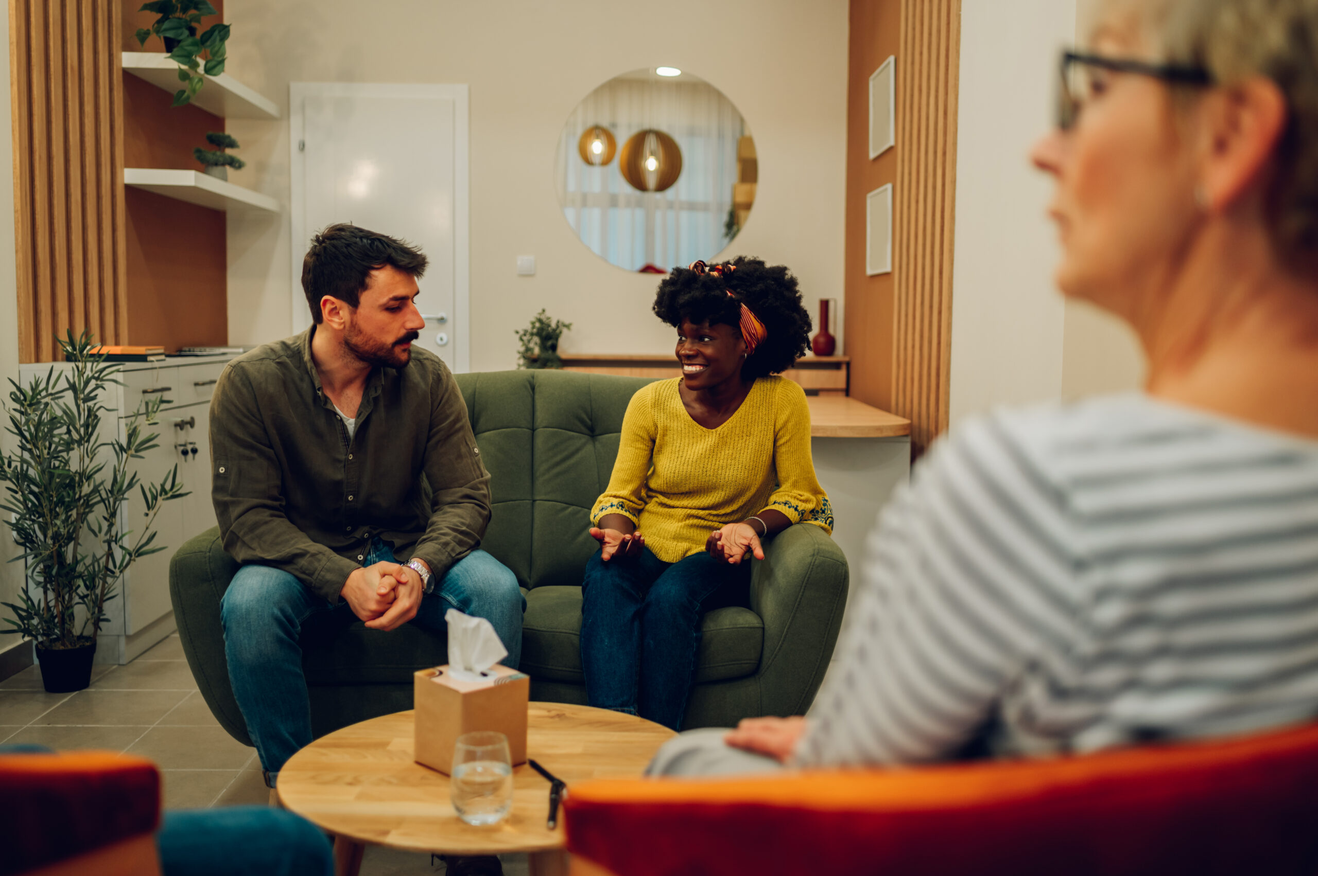 African american woman supporting new attender of group therapy to talk about himself during a meeting at mental health center. Group therapy participants sitting in a circle and talking.