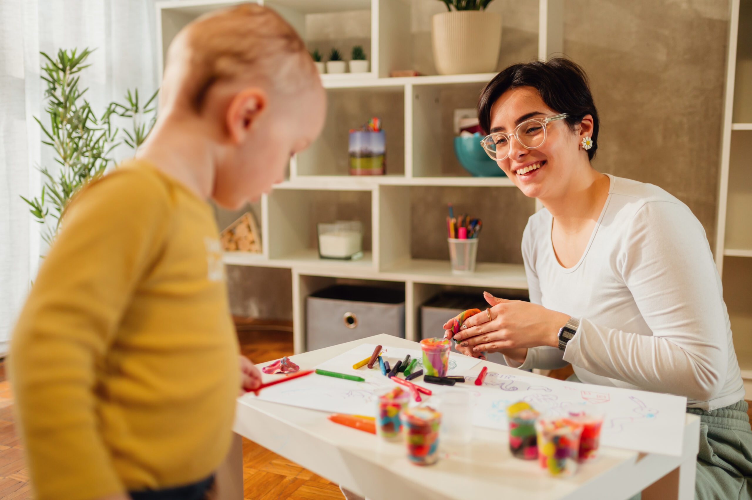 Family of two improving fine motor skill trough the games while coloring with crayons. Toddler boy playing with his mother or aunt. Funny educational games for children. Focus on a mother.