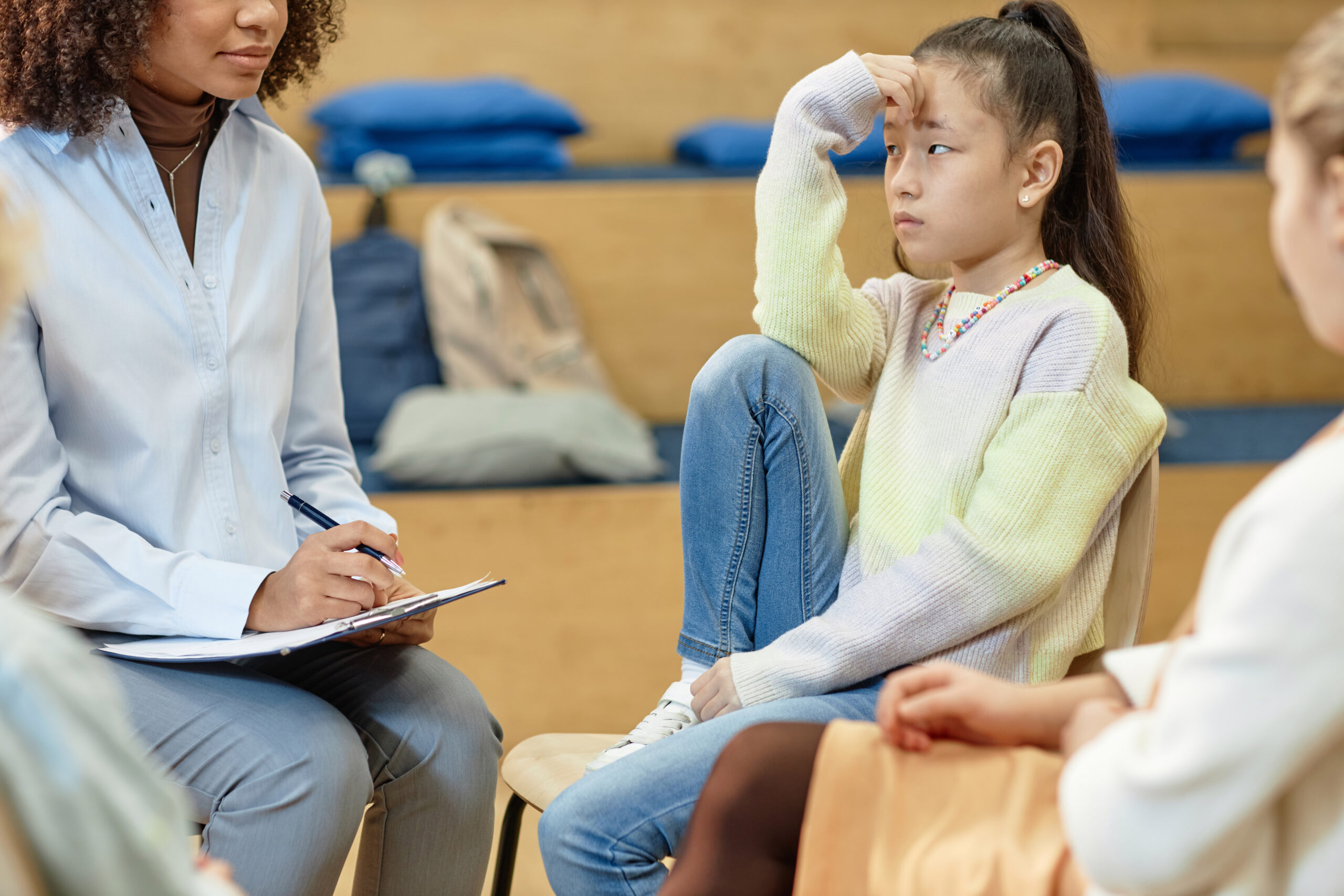 Side view portrait of Asian teenage girl listening to female psychologist in support group meeting for children